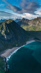 Stunning aerial perspective of Ryten Kvalvika beach trail, showcasing lush green mountains, vibrant blue ocean waves, and sunny skies. Ideal for nature lovers and outdoor adventure enthusiasts.
