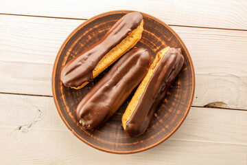 Chocolate sweet eclairs with clay plate on wooden table, macro, top view.