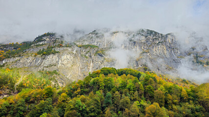 Majestic mountain landscape with vibrant autumn foliage, shrouded in mist, showcasing rocky cliffs and lush greenery, creating a serene natural atmosphere in the wilderness