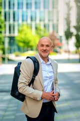 Confident middle-aged man walking along a city street and holding laptop in his hand