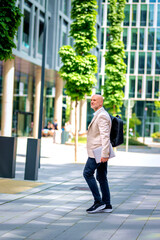 Confident middle-aged man walking along a city street and holding laptop in his hand