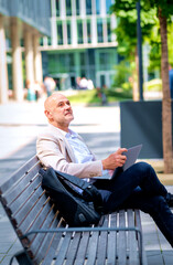 Businessman relaxing on a bench in a city environmental and using laptop