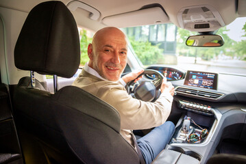 A middle-aged man sitting in his car, hands on wheel and looking back
