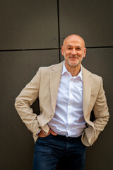 A middle-aged man standing in front of a grey wall outdoor and looking at camera and smiling