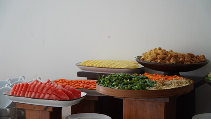A colorful buffet spread featuring large platters of sliced watermelon, carrots, and various...