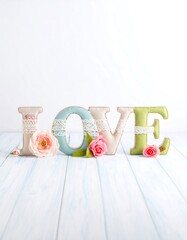 Pastel-colored letters spelling "LOVE" adorned with lace and flowers on a light blue wooden background