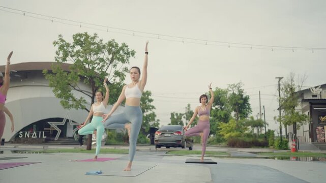 Women stretch upward in a yoga class, performing a standing pose together under soft morning light outdoors.