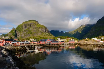 Keuken achterwand Lofoten A Lofoten village showcases traditional red fishing cabins along the waterfront, surrounded by majestic mountains under a partly cloudy sky. A perfect blend of nature and culture.  © Fokke Baarssen