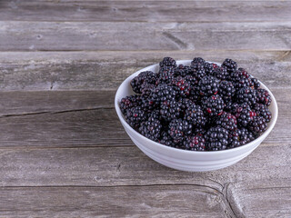 Fresh ripe blackberries in white ceramic bowl on rustic wooden table, organic summer fruit.
