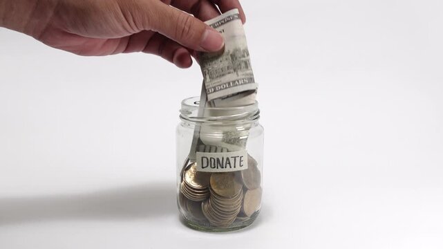 Depositing banknotes into a jar labeled Donate filled with cash and coins, symbolizing generosity, fundraising, and charitable giving