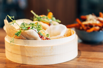 Steamed Asian bao buns served in a bamboo basket with fresh garnish in a trendy restaurant