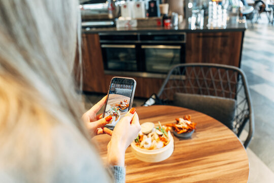 Woman Taking a Smartphone Photo of a Restaurant Dish at a Wooden Table