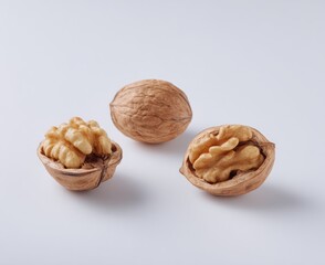 Trio of walnuts on a stark white background, one whole and two split open, showcasing their shelled interior details under soft, natural light