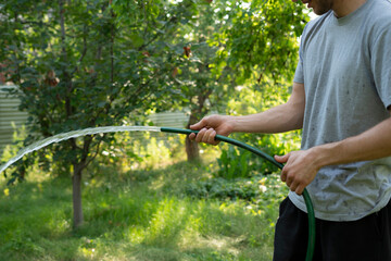 Individual holds a green hose, watering the grass in a vibrant garden setting full of healthy...