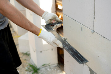 A worker holds an angle ruler against a wall at a construction site, focusing on accurate measurements to ensure correct alignment during the building process.