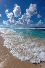 Turquoise ocean waves gently roll onto a sandy beach under a bright blue sky dotted with fluffy white clouds on a sunny day