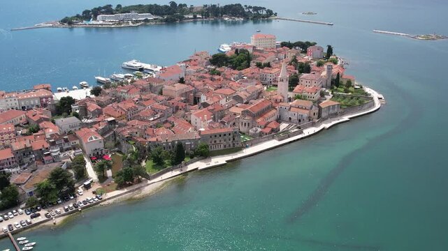 Aerial drone view of Porec Old Town and the Euphrasian Basilica on the Istrian coast of Croatia. The red-tiled roofs and historical buildings rest along the scenic Adriatic shoreline with marina.