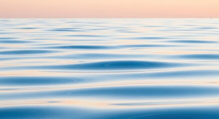 Fototapeta premium Gentle ripples on a calm ocean surface reflecting a soft sunrise sky