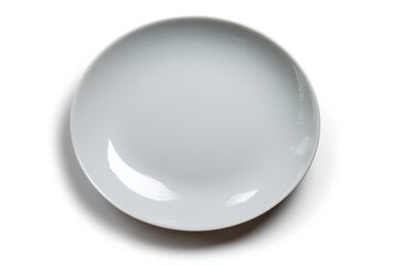 An overhead studio shot of a pristine, empty, white porcelain plate against a stark white backdrop, casting a subtle shadow, emphasizing its concave form