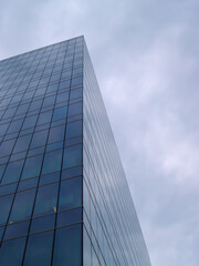 Obraz premium Modern glass skyscraper facade with reflective windows and cloudy sky