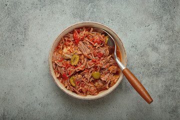 Ropa vieja, a traditional Cuban dish, is served with white rice, tomato sauce, and green olives on a plate from above on grey rustic background