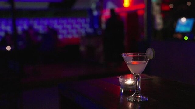 A stylish cocktail glass with an elegant mixed drink displayed on a bar counter in a modern night bar. Neon lights, bokeh, and moody low-light atmosphere create a sophisticated nightlife vibe. Perfect