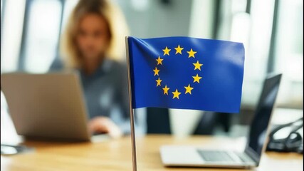 An office environment features a European flag prominently displayed with a person working on a laptop in the background. Focused discussions and collaboration are evident. - Powered by Adobe