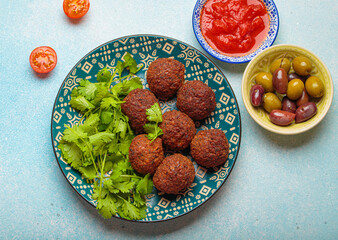 Delicious homemade falafel balls served on a beautiful patterned plate with fresh coriander, tomato sauce and green olives, a vibrant and appetizing middle eastern meal