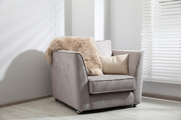 Comfortable armchair, fluffy blanket and cushion in light room
