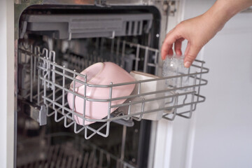Hand loading pink bowl and glass into dishwasher rack in modern kitchen setting.