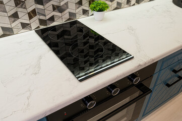 Modern kitchen detail: black stovetop on marble counter, with a black oven below. Geometric tiles...