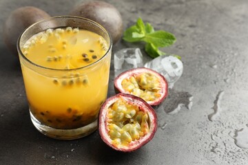 Tasty passion fruit drink with mint, ice cubes and fresh fruits on grey table, closeup. Space for text