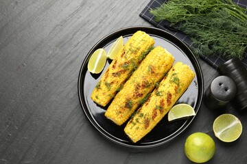 Tasty grilled corncobs with dill and lime slices on black table, flat lay