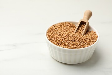 Dry mustard seeds in bowl and scoop on white marble table, closeup. Space for text