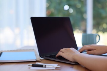 Woman working with laptop at table against blurred background, closeup