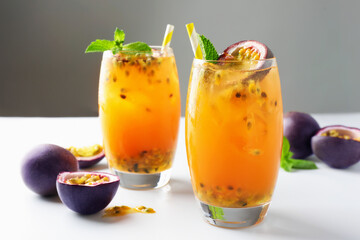 Tasty passion fruit drink with mint in glasses and fresh fruits on light table against gray background, closeup