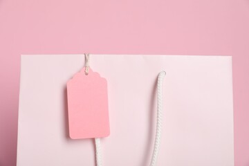 Shopping bag with blank tag on pink background, closeup