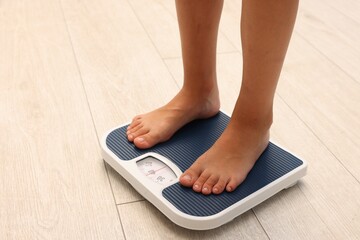 Little boy standing on scales indoors, closeup. Space for text
