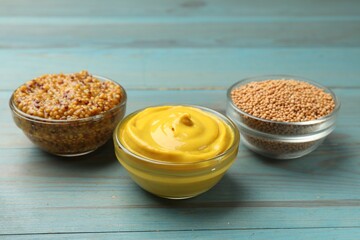 Different types of mustard on light blue wooden table, closeup