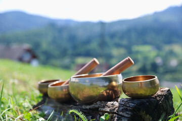 Tibetan singing bowls with mallets on piece of wood outdoors