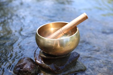 Tibetan singing bowl with mallet on stone near river, closeup