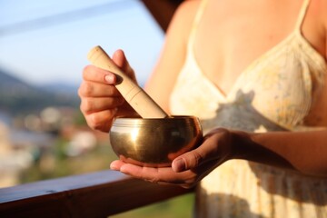Woman with singing bowl outdoors on sunny day, closeup