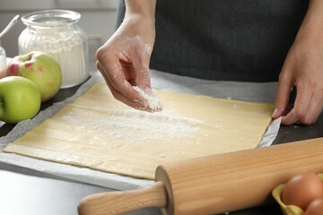 Making delicious apple strudel. Woman sprinkling flour onto dough at grey table in kitchen, closeup