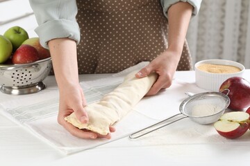 Woman making delicious apple strudel at white wooden table in kitchen, closeup