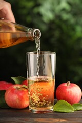 Woman pouring delicious cider into glass at wooden table outdoors, closeup