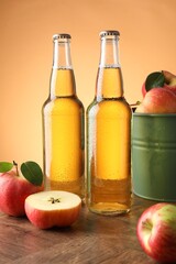 Delicious cider in glass bottles and apples on wooden table against orange gradient background