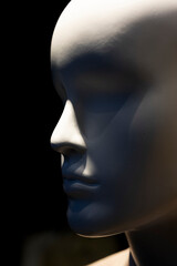 Close-up detail of a mannequin's face in a shop window with strong shadows and lights.