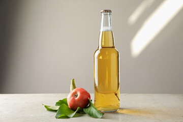 Delicious cider in glass bottle and apples on gray table against light background