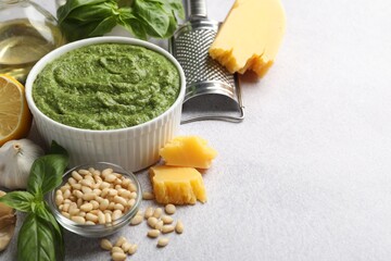 Fresh pesto sauce in bowl and ingredients on light grey table, closeup. Space for text