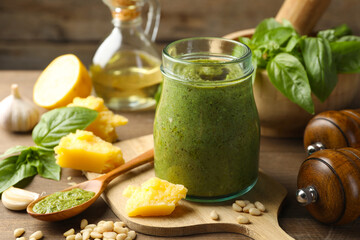 Fresh pesto sauce in jar and ingredients on wooden table, closeup